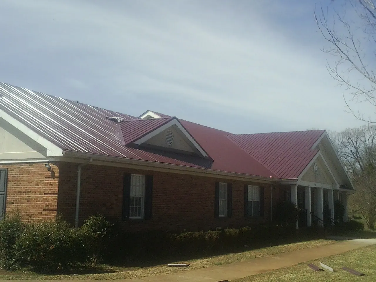 Red metal roof with gabled entries on a long brick building, from a Hail Damage Roof Repair job in Tieton