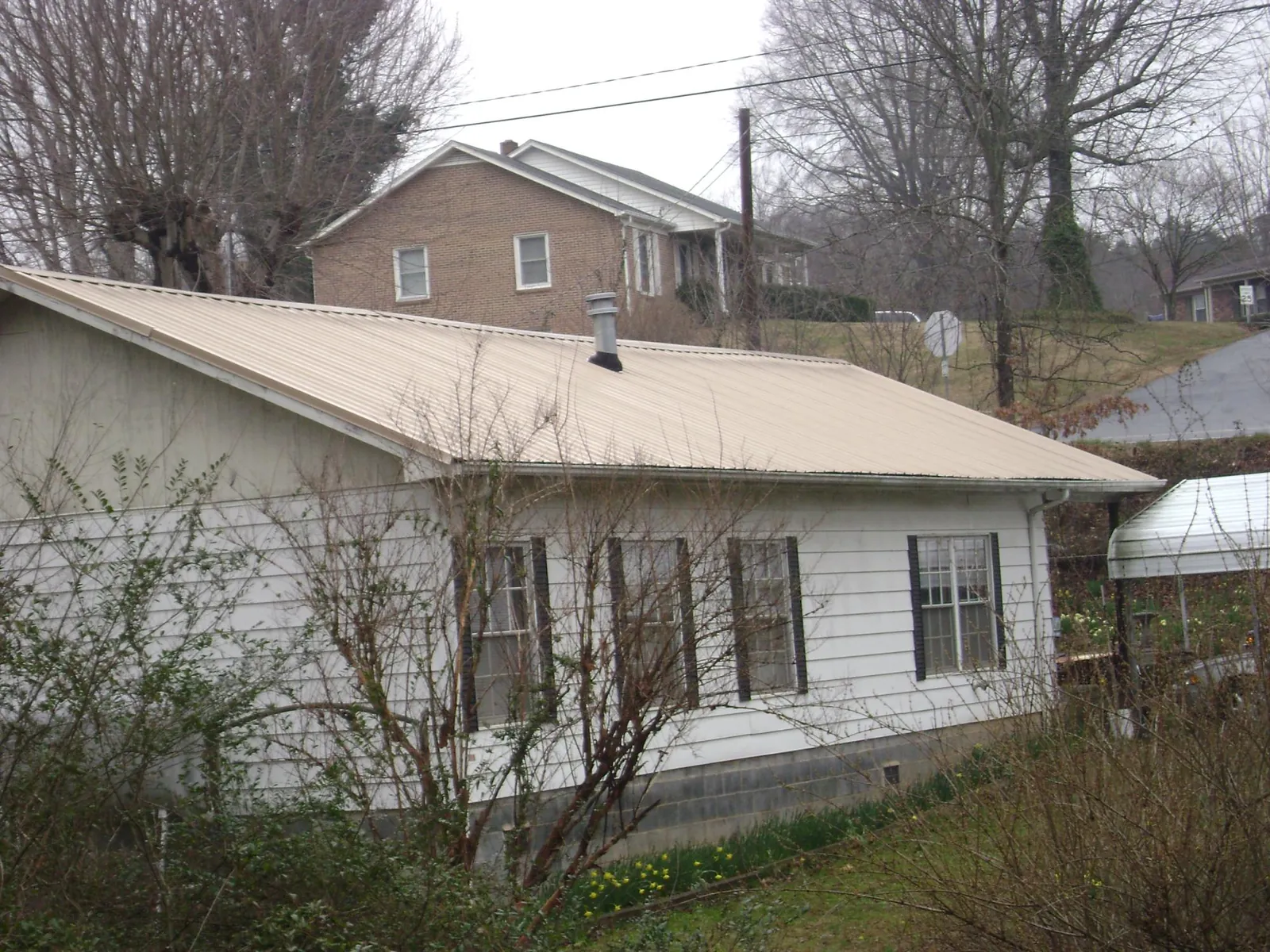 Tan metal roof on a white sided house set into a hillside — Commercial Roofing by Roofing Brothers in Tieton